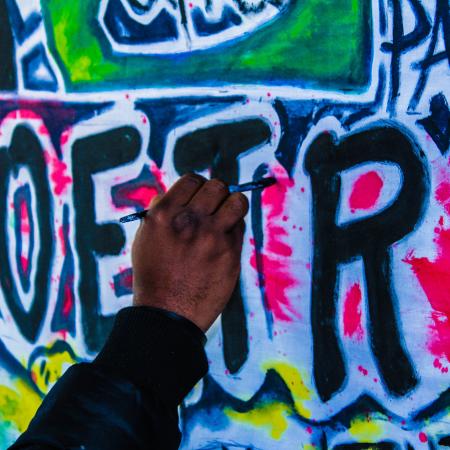 A black man's hand is painting the word "poetry" on a wall, graffiti style