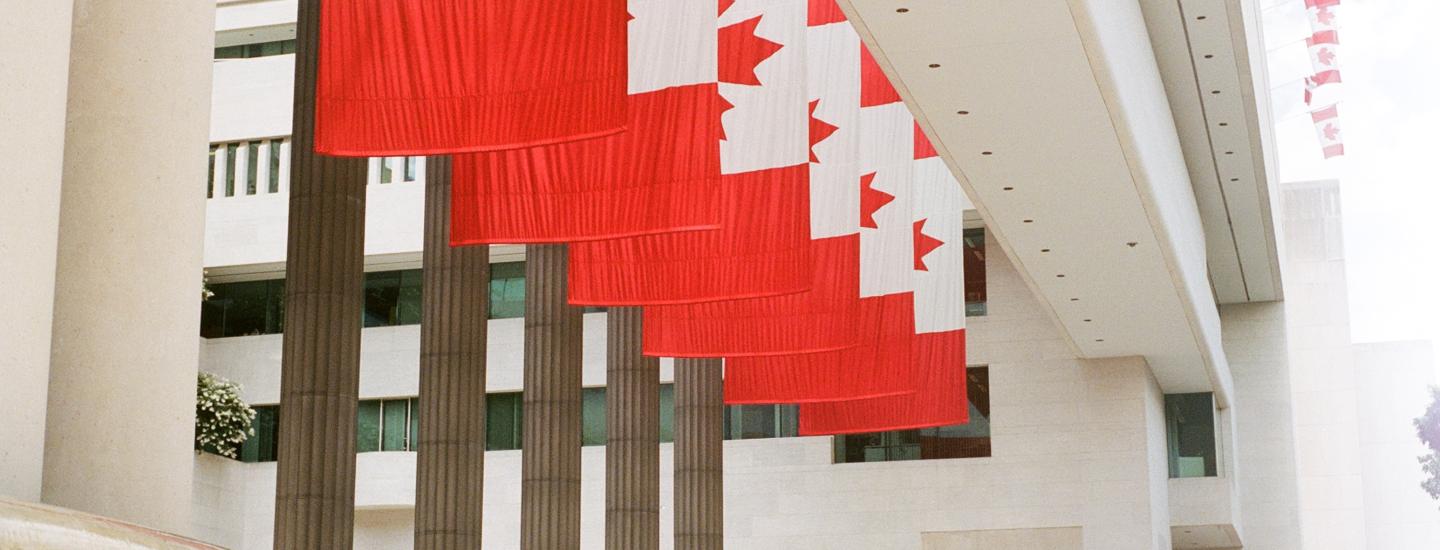A row of Canadian flags hang in front of a building staircase