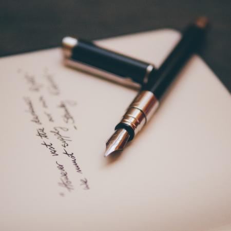 An ornate green and gold pen lies on an open page with blurry cursive text. 